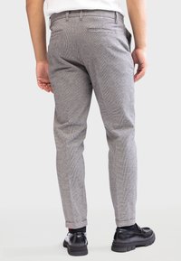 Pantalons à carreaux gris avec une coupe slim, passants de ceinture et deux poches arrière. Portés avec des chaussures noires, montrant une texture lisse.