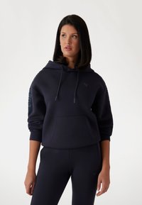 Hoodie marine foncé en matériau doux, avec une poche avant, des cordons ajustables et des accents texturés sur les manches.