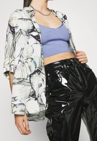 Květinová košile ve velkém střihu v bílé, fialové a zelené barvě, přeložená přes světle modrý žebrovaný crop top, v kombinaci s lesklými černými kalhotami s vysokým pasem.
