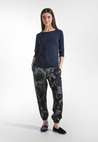 Granatowa bluzka z rękawami długości 3/4, szare spodnie dresowe w kwiatowy wzór oraz ciemne wsuwane buty. Materiał wydaje się miękki; spodnie dresowe mają elastyczne mankiety i kieszenie.