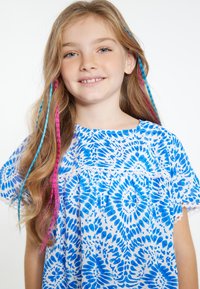 Camicia bianca con motivo floreale blu, maniche corte e rifiniture in pizzo. I capelli presentano ciocche di toni blu e rosa.