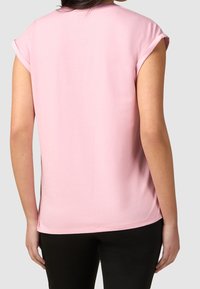 Haut rose à manches courtes en tissu doux, avec un col rond et des manches retournées, vu de dos sur un fond neutre.