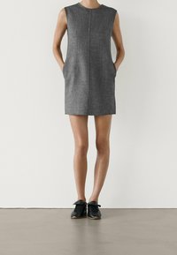 Robe sans manches grise au design simple, dotée de poches, à coupe droite et à texture lisse. Associée à des baskets noires.