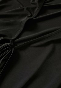 Tissu noir avec de doux plis et un détail de couture froncée créant texture et profondeur sur un matériau lisse.