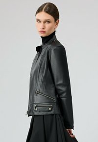 Zwarte leren jas met ritszakken, gestructureerde afwerking, asymmetrisch ontwerp en metalen hardwareaccenten; aansluitende silhouet.