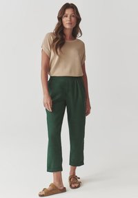 Haut beige à manches courtes et pantalon décontracté vert foncé, associés à des sandales marron. Tissu lisse, design décontracté, pantalon jusqu'aux genoux.