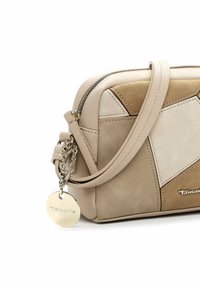 Beige läder- och mockabandsväska med geometriska lappar, dragkedjestängning, avtagbar kedjeprydnad och ett runt tag som är graverat med "Tamaris."