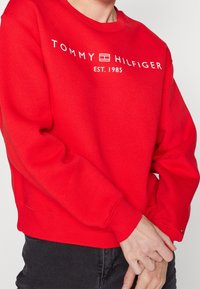 Czerwona bawełniana bluza z okrągłym dekoltem, ściągaczami na mankietach i u dołu. Na klatce piersiowej nadrukowane białe logo "TOMMY HILFIGER EST. 1985".