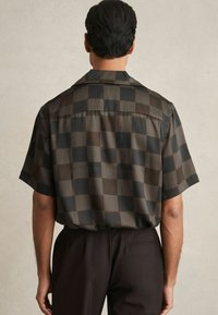 Camisa de manga corta con un patrón a cuadros oscuro, fabricada en un tejido suave y brillante, con un corte relajado y detalle de yugo en la parte posterior.