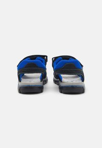Rückansicht verstellbarer Sandalen mit blauen und schwarzen Wildlederriemen, gepolstertem Innenbereich und einer strukturierten Gummisohle für optimalen Grip.
