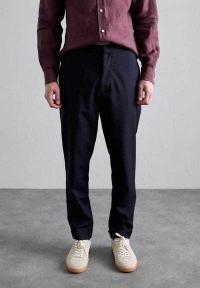 Pantaloni cremu din stofă ușoară, cu un croi drept și buzunare laterale. Purtați cu adidași bej cu talpă joasă.