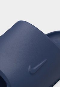 Gros plan sur une sandale Nike bleu marine avec une surface texturée et le logo Nike en relief sur la bride.