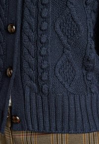 Jūras spēku adīts džemperis ar adījuma rakstiem un ribotām piedurknēm. Pabeigts ar tumšām pogām un teksturētu audumu. Piemērots slāņu veidošanai.