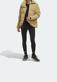 Kuklovaná bunda v světlé hnědé barvě, s límcem na zip a patentkami. V kombinaci s černými legínami a tmavými sportovními botami.