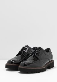 Blanklædte sorte lædersko med snørre, vinge-design, brogue-detaljer og en tyk struktureret sål for godt greb. Velegnet til både formelt og afslappet brug.