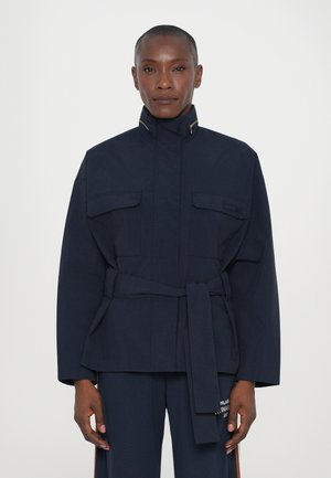Parka bleu marine avec un col haut, une taille ceinturée et quatre poches avant. Fabriquée en tissu lisse, elle présente un design minimaliste.