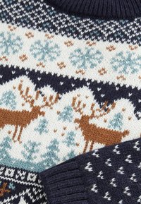 Strickpullover mit hellem Grundton und Mustern in Marineblau, Türkis und Braun, darunter Rehe und Schneeflocken. Gerippte Ärmelbündchen in Marineblau.