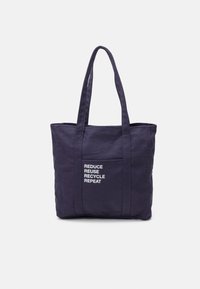 Sac fourre-tout en toile bleu marine avec deux poignées robustes, une poche avant et un texte blanc indiquant "RÉDUIRE REUTILISER RECYCLER RÉPÉTER." Design simple.