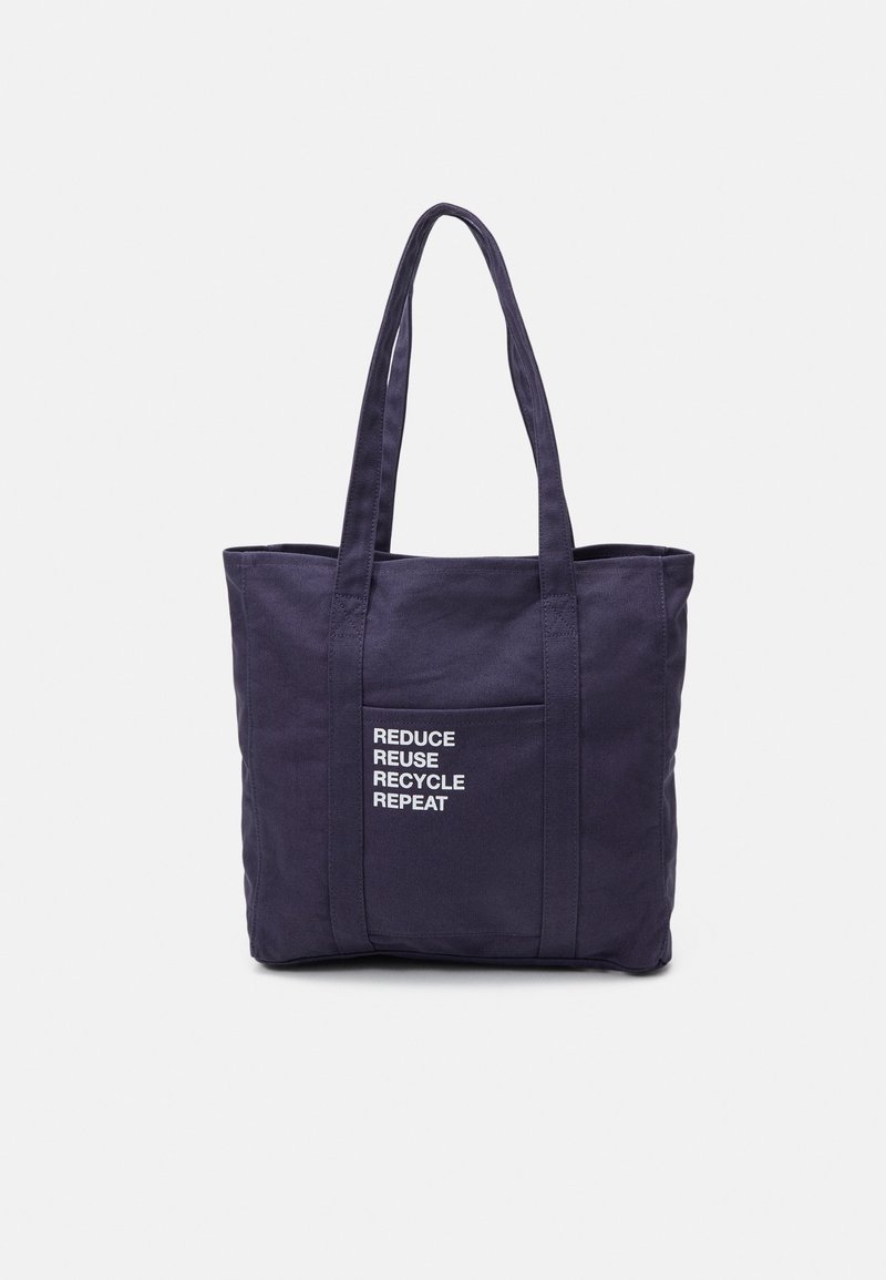 Sac fourre-tout en toile bleu marine avec deux poignées robustes, une poche avant et un texte blanc indiquant "RÉDUIRE REUTILISER RECYCLER RÉPÉTER." Design simple.