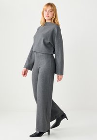 Ensemble gris en deux pièces comprenant un haut à manches longues ample et un pantalon taille haute à jambes larges. Tissu texturé et escarpins noirs pointus.