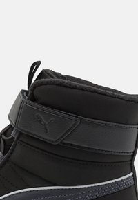 Zwarte enkelboot met een ronde neus, synthetisch bovenwerk, gevoerde schacht, klittenbandsluiting en contrasterende grijze stiksels langs de zool.
