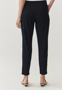 Pantaloni blu navy con una vestibilità su misura, dotati di un orlo a risvolto e due tasche posteriori. Realizzati in un tessuto liscio e strutturato.