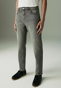 Szare dżinsy o slim fit, pięć kieszeni, delikatne przetarcia i zamek błyskawiczny. W komplecie z czarnymi sznurowanymi butami.