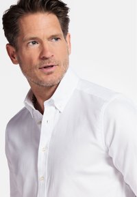 Chemise blanche à manches longues avec un motif texturé subtil, dotée d'un col classique et de boutons standards. Design épuré et ajusté.