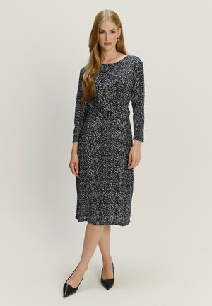 Granatowa sukienka w kwiaty z długimi rękawami, elastyczną talią i długością do kolan. Para czarnych szpilki z ostrym noskiem uzupełnia outfit.