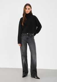 Schwarzer Rollkragenpullover, verkürztes Design, gerippter Saum. Kombiniert mit hochgeschnittenen grauen weiten Jeans, abgerundet mit schwarzen spitzen Schuhen.