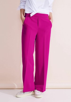 Fuchsiaweite Hosen mit weitem Bein und flacher Vorderseite, zwei Seitentaschen, kombiniert mit weißen Sneakers. Glatter Stoff mit minimalen Akzenten.