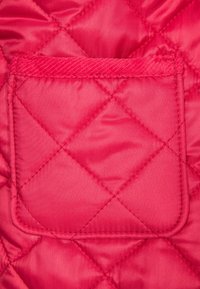 Růžová prošitá látka se vzorem diamantů, vybavená malou náprsní kapsou s prošitým okrajem, představující hladkou, lesklou texturu.