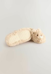 Chausson en fausse fourrure beige avec un design d'ours, texture douce, oreilles rondes et semelle souple avec le nom de la marque en relief.