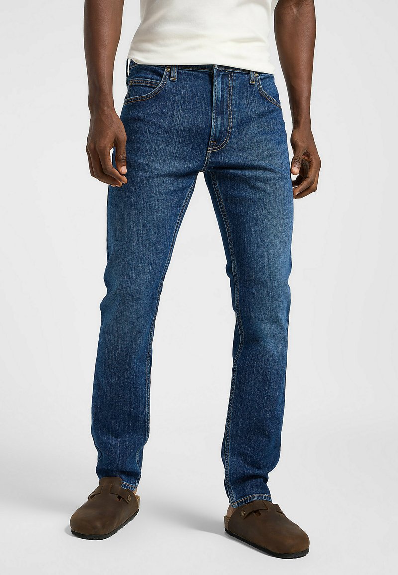 Vaqueros de mezclilla azul oscuro con corte recto, con diseño de cinco bolsillos, un ligero desvanecimiento y una cintura de altura media. Llevados con zuecos marrones.