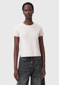 Maglione corto rosa chiaro a maniche corte in un tessuto morbido con scollatura rotonda. Indossato con jeans in denim scuro a vita alta. Lunghezza cropped, design minimale.