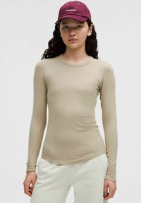 Camicetta beige a maniche lunghe in un design aderente, realizzata in tessuto morbido. Presenta un colletto rotondo e una leggera arricciatura all'orlo.