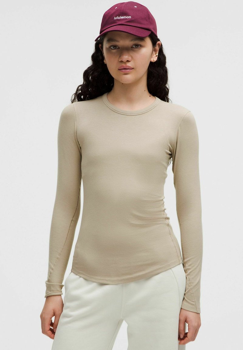 Camicetta beige a maniche lunghe in un design aderente, realizzata in tessuto morbido. Presenta un colletto rotondo e una leggera arricciatura all'orlo.