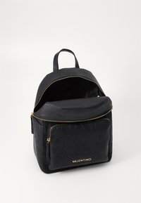 Crna kožna ruksak s teksturiranim brendingom, dvostrukim rajsferšlusima i ručkom na vrhu. Sadrži jedan veliki odjeljak i prednji džep s rajsferšlusom.