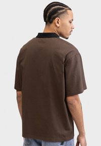 Brown short-sleeve polo shirt with a black collar, made of a soft material, featuring a relaxed fit and simple design.