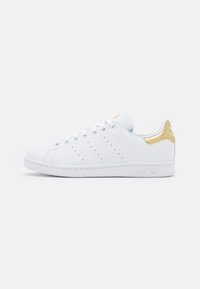 Vita Adidas Stan Smith-sneaker med guldhäll, vita snören och perforerad tre-stripe-design på sidan.