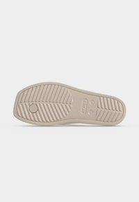 Σόλα από μια μπεζ Crocs με υφή για καλύτερη πρόσφυση και κυκλικό σχέδιο κοντά στη φτέρνα, ορατές σημάνσεις μεγέθους στην περιοχή της καμάρας.