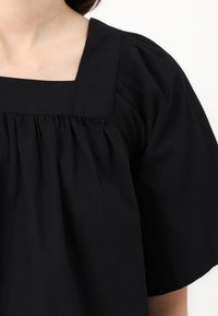 Top nero a maniche corte con scollo quadrato e dettaglio di tessuto arricciato. Realizzato in un materiale morbido e strutturato.
