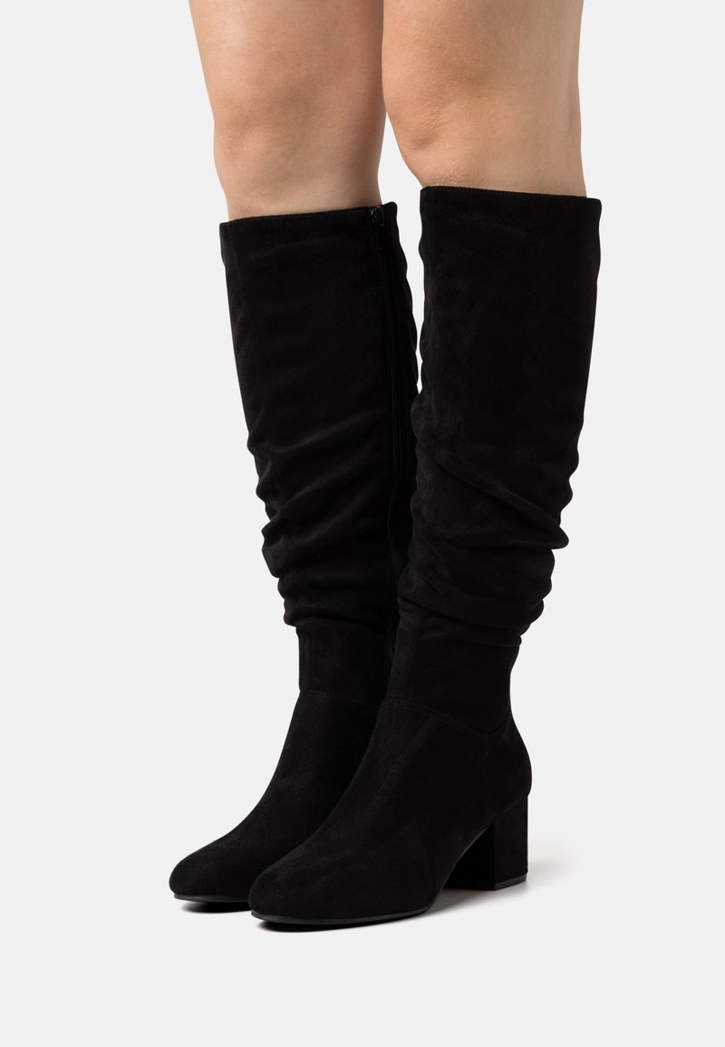 Bottes hauteur genou en daim noir avec un design décontracté, talon carré épais et fermeture éclair latérale pour un enfilage facile. Texture lisse et détails minimalistes.