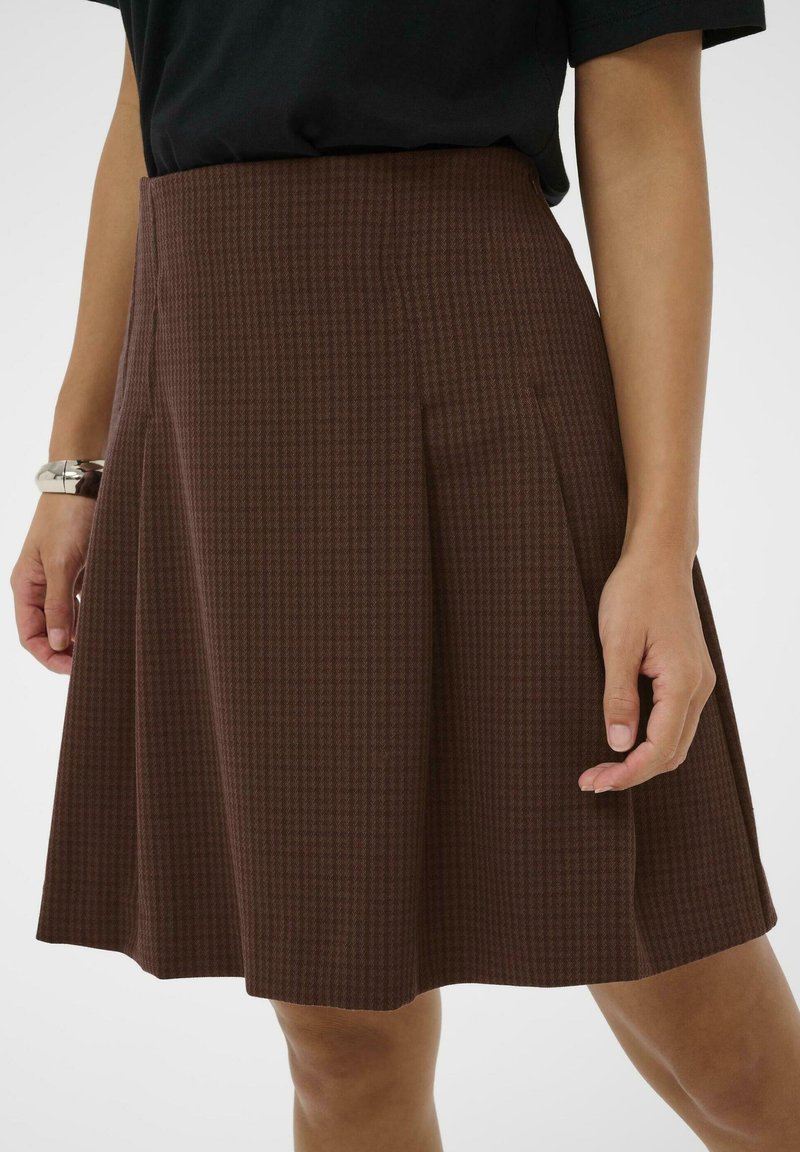 Jupe à carreaux marron avec un design plissé, fabriquée en tissu texturé. L'ourlet tombe au-dessus du genou, avec des poches latérales et une taille ajustée.