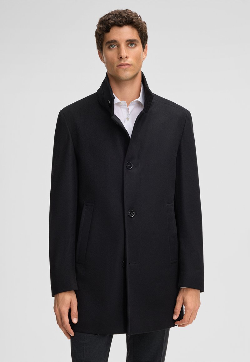 Cappotto di lana nera con colletto alto, chiusura frontale a bottoni e tasche laterali. Texture liscia e silhouette sagomata, adatto per abbigliamento formale.
