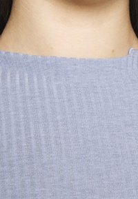 Světle modrý ribbed pletený top s texturovaným povrchem, který má kulatý výstřih a jemné variace v odstínu po celé délce.
