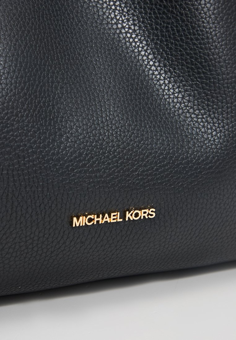 Close-up van zwart gewatteerd leer met het glanzende gouden "MICHAEL KORS" logo dat gecentreerd op het oppervlak staat.