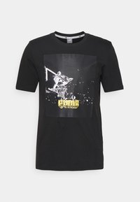 Sort bomulds T-shirt med korte ærmer, der har et grafikprint af en kat, der spiller basketball, fremhævet af gul tekst nedenfor.