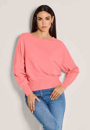 Korallefarbener gestrickter Pullover mit lockerer Passform, weitem Rundhalsausschnitt, langen Ärmeln und geripptem Saum, kombiniert mit blauen Jeans.