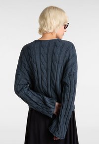 Cable-knit sweater in dark blue, featuring textured ridges and loose-fit sleeves. Rounded neckline with a relaxed silhouette.